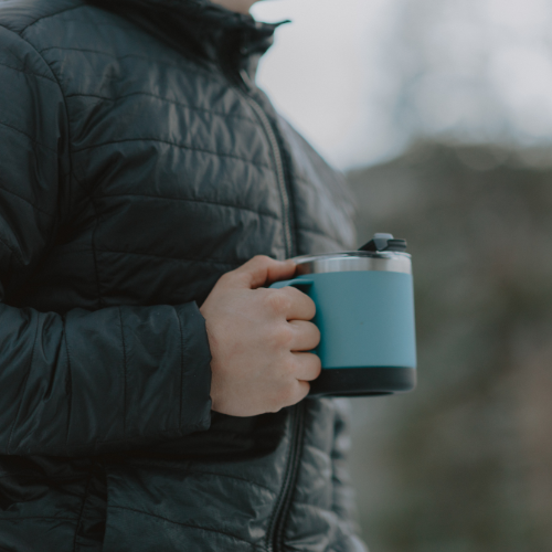 Male camper wearing a jacket and holding a Cordova Outdoors Trailhead Class 14 oz insulated mug