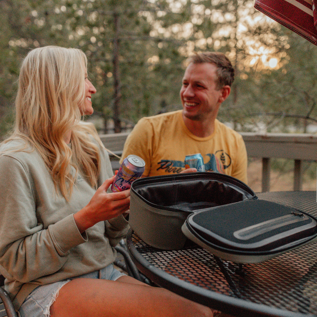 A woman and man enjoying cold drinks on a patio from a scree gray Cordova insulated cooler lunch bag. [Scree]